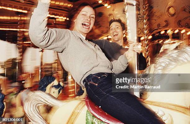 young couple riding on carousel, close-up (blurred motion) - carousel horses stock-fotos und bilder