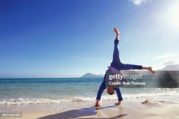 young man wearing suit, doing cartwheel on beach - cartwheel stock pictures, royalty-free photos & images
