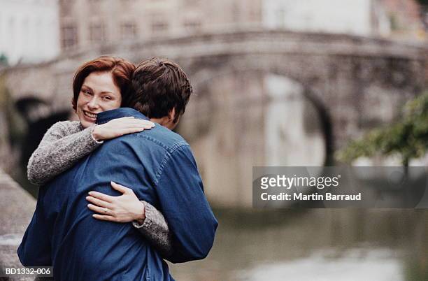 young couple embracing beside canal, bruges, flanders, belgium - bruges stockfoto's en -beelden