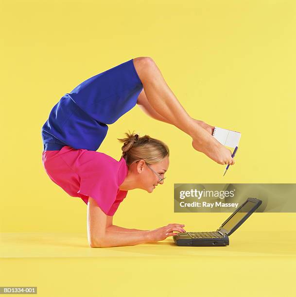 young woman using laptop on floor, holding notepad and pen with feet - young contortionist stockfoto's en -beelden