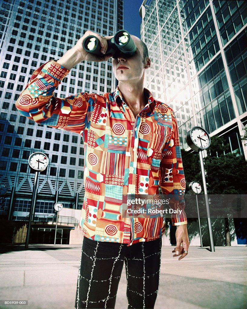Young man with binoculars, standing in urban environment (Composite)