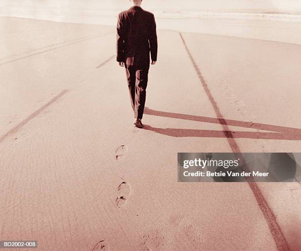 businessman walking on beach between road markings (toned b&w) - midlife crisis stock pictures, royalty-free photos & images