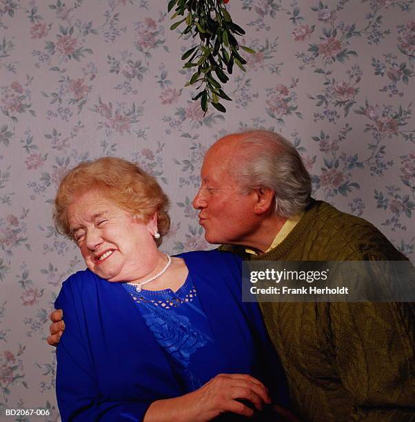mature couple under mistletoe, man kissing woman, woman grimacing - couple de vieux drole photos et images de collection