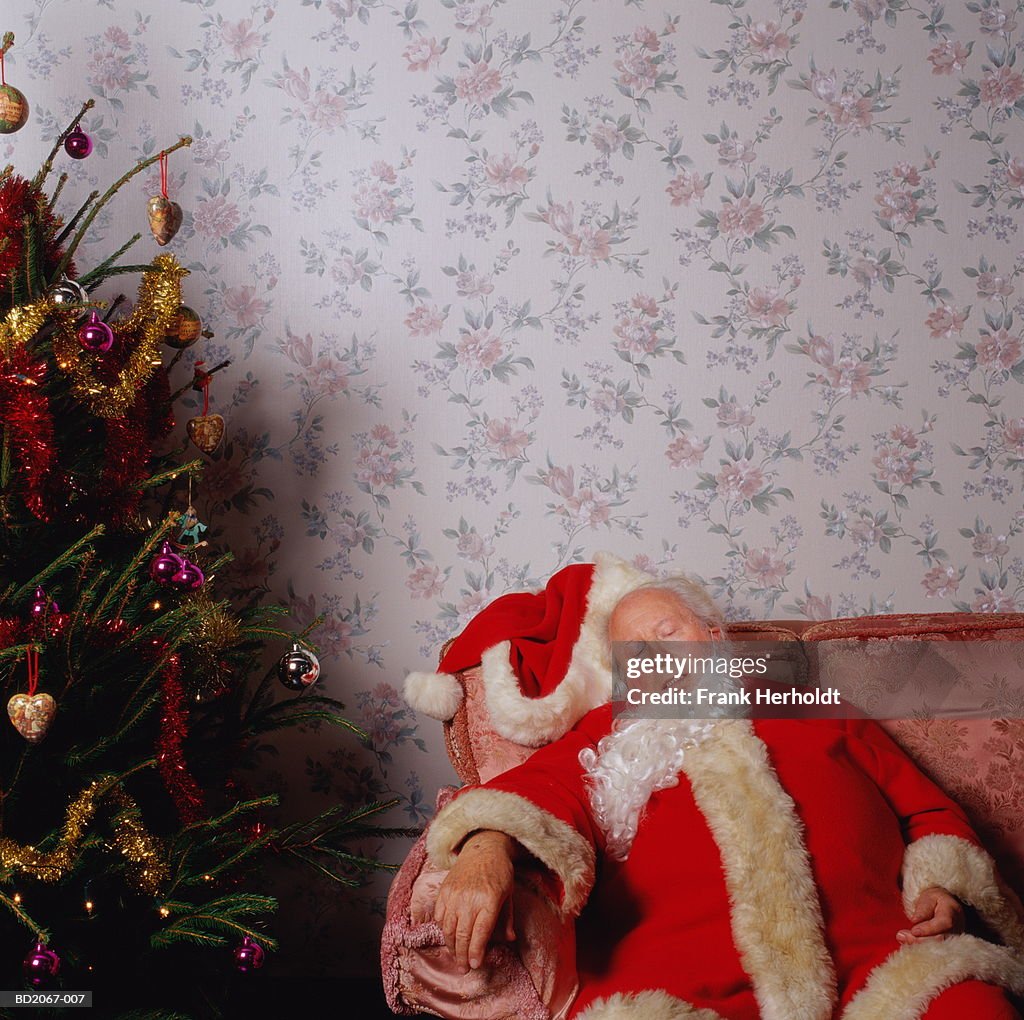 Father Christmas asleep on sofa, next to Christmas tree