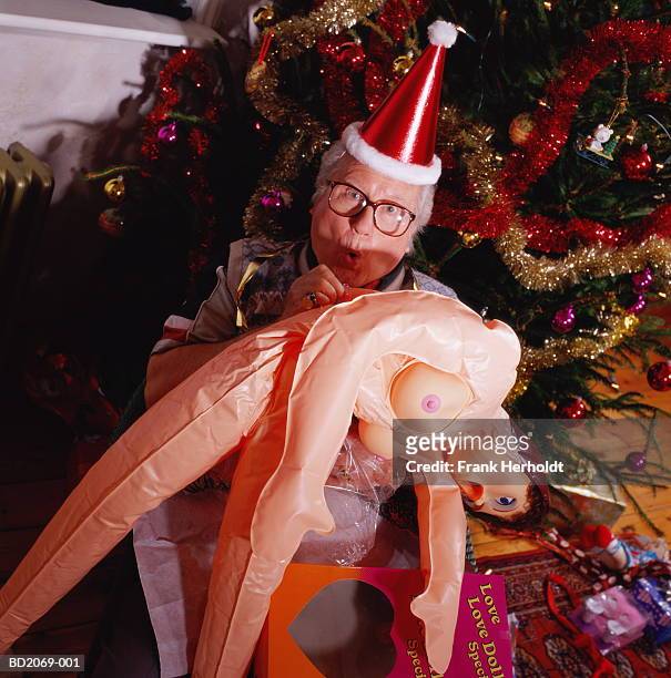 mature man in front of christmas tree, blowing up inflatable doll - mann gummipuppe stock-fotos und bilder
