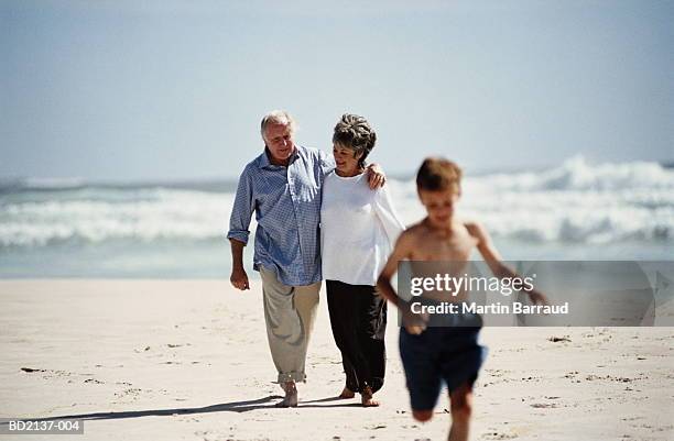 mature couple and boy (7-9) walking along sandy beach - northern european descent stock pictures, royalty-free photos & images