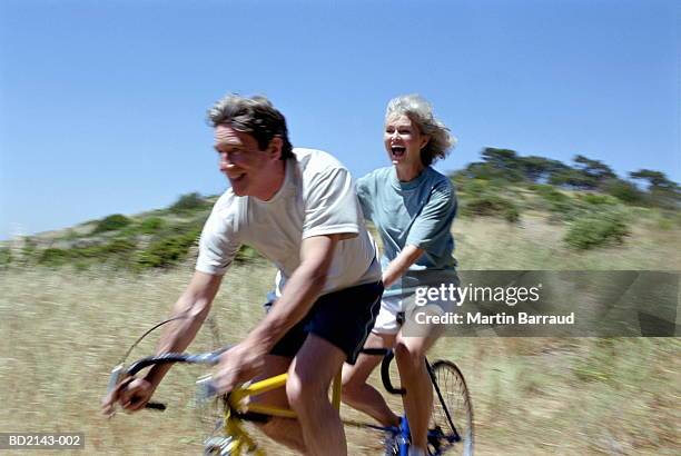 mature couple riding tandem, smiling (blurred motion) - tandem stock pictures, royalty-free photos & images