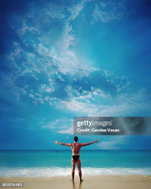 man standing on beach, arms outstretched, rear view - calções de corrida imagens e fotografias de stock