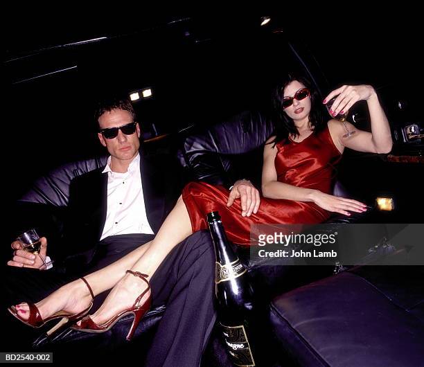 couple drinking champagne on back seat of limousine - privilegien stil stock-fotos und bilder