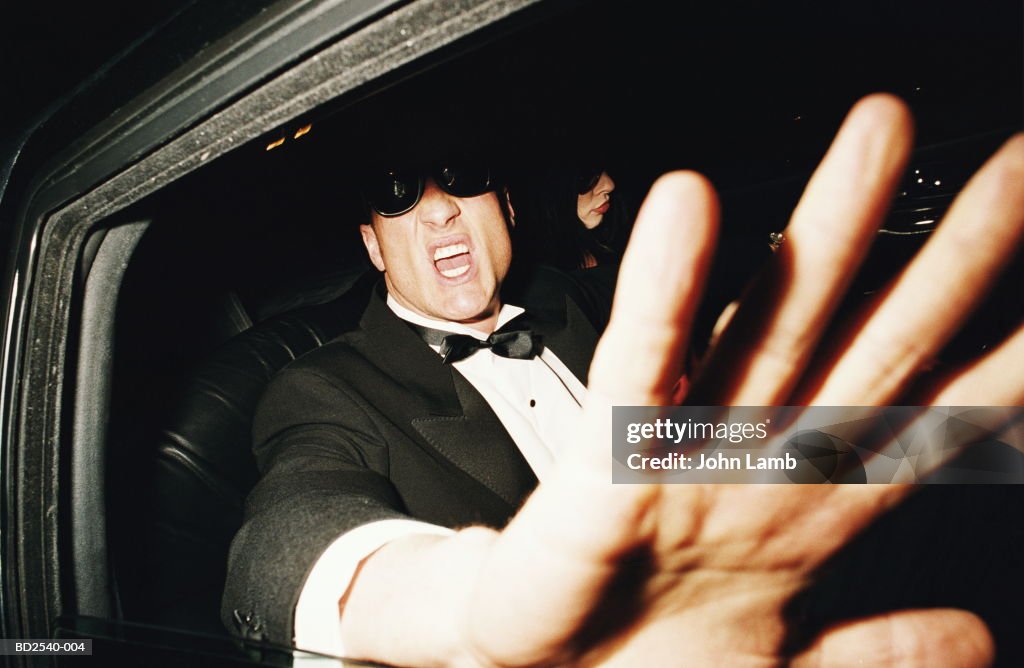 Man in back of limousine raising hand to camera, close-up