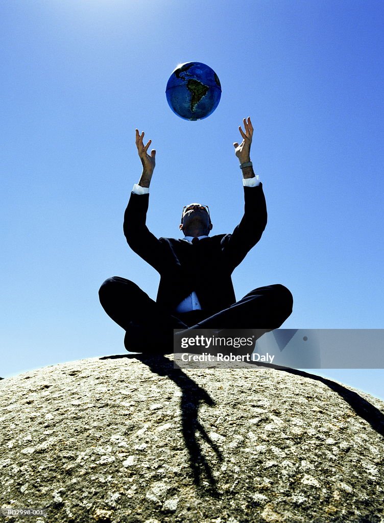 Male executive sitting, throwing globe up in air, low angle view