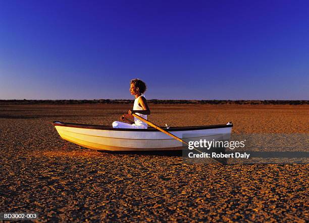 young man sitting in rowing boat in middle of desert (cross-processed) - 划艇 個照片及圖片檔