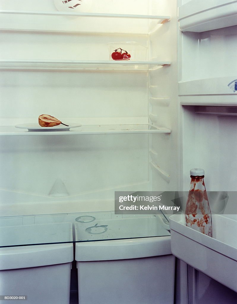 Refrigerator with empty ketchup bottle and old pear, close-up