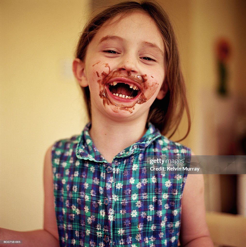 Girl (5-7) with chocolate smeared over face, smiling, portrait