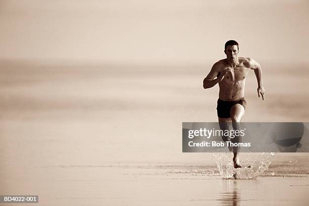 young man running along beach (toned b&w) - young men in speedos stock-fotos und bilder