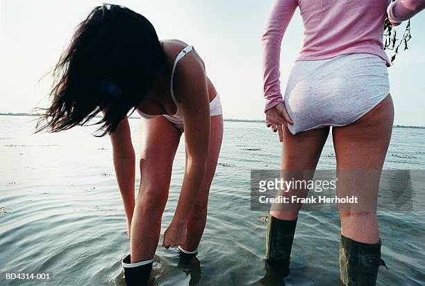 two young women in underwear and wellington boots, paddling in sea - leaning over stock-fotos und bilder