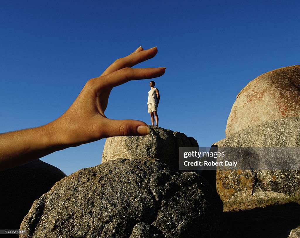 Man standing on rock, hand sizing him in foreground (Composite)