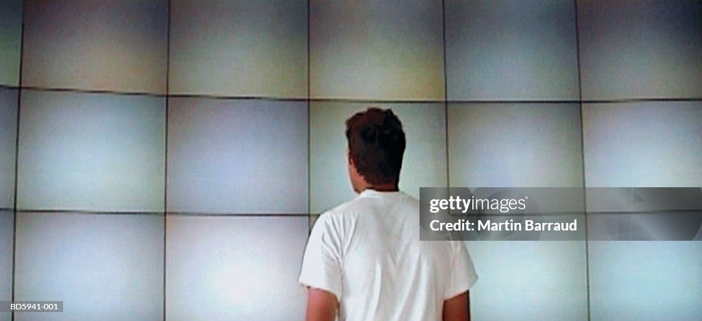Man looking at wall of monitors, rear view (video still)