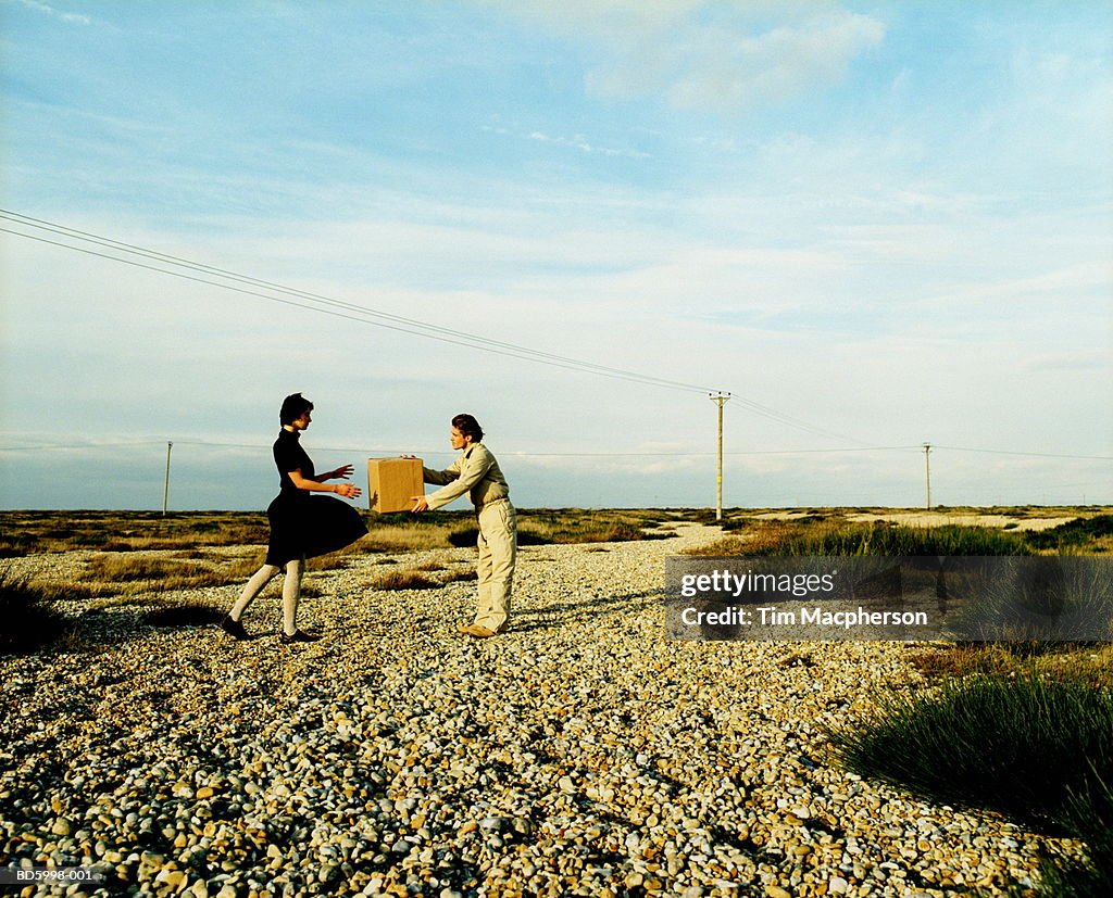 Couple on road in landscape, man passing box to woman