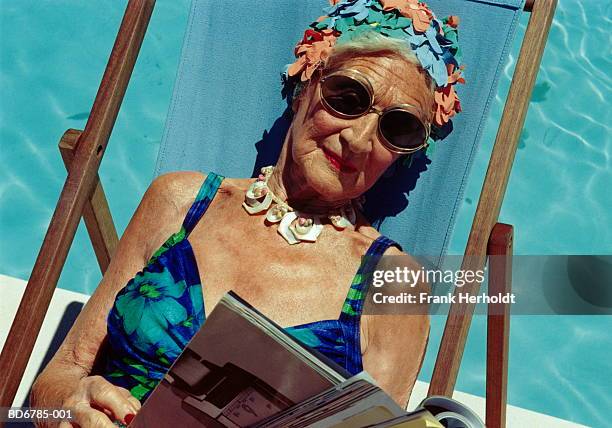 elderly woman in deckchair by pool, reading magazine, close-up - old woman in swimsuit stock-fotos und bilder