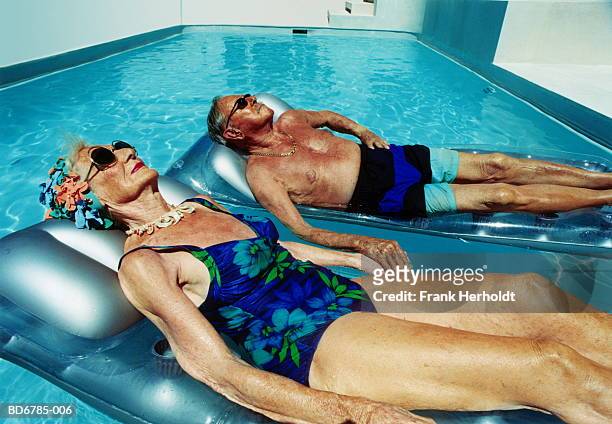 elderly couple lying on inflatables in pool - quemado por el sol fotografías e imágenes de stock