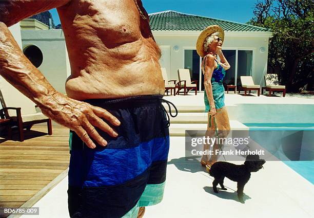 elderly couple and black poodle standing by pool - old woman in swimsuit stock-fotos und bilder