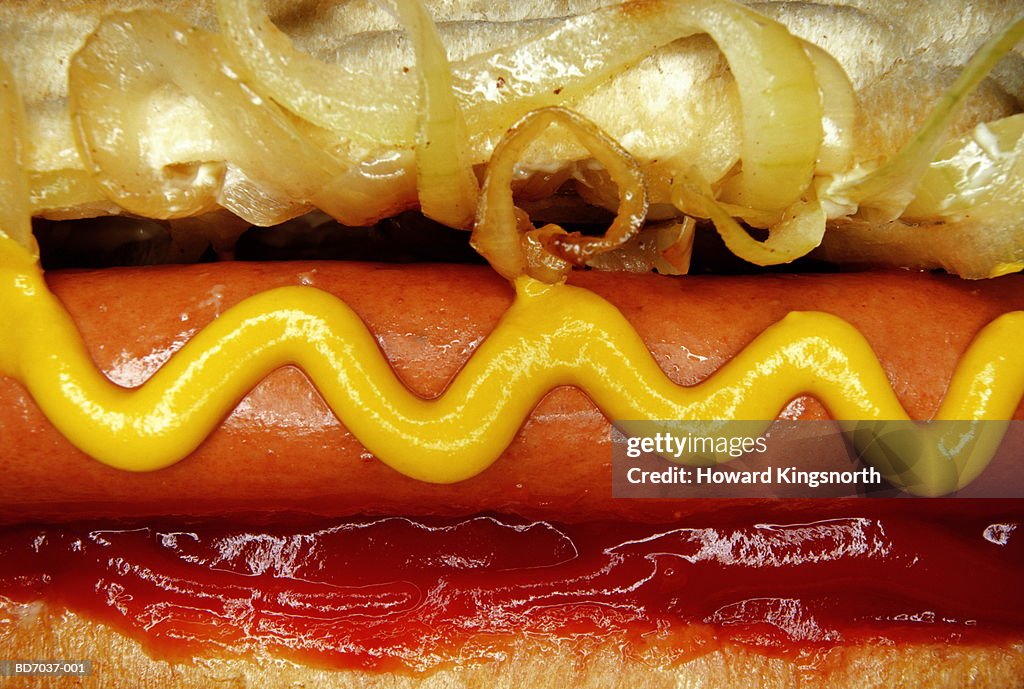 Hotdog with mustard, tomato ketchup and onions, close-up