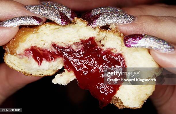 woman with long glittery nails eating jam doughnut, close-up - long fingernails imagens e fotografias de stock