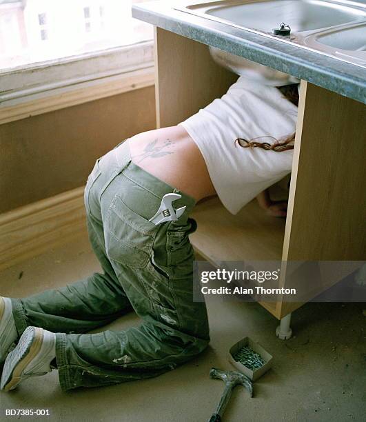 young woman fixing sink, spanner in  back pocket - lower house stock pictures, royalty-free photos & images