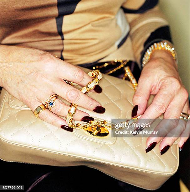 mature woman holding handbag, close-up - gold nail polish stock-fotos und bilder