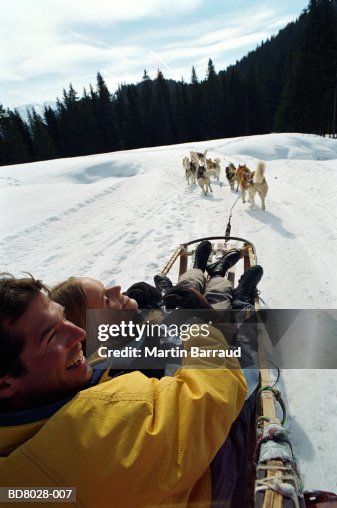 Couple on sledge being pulled by Huskies, over shoulder view