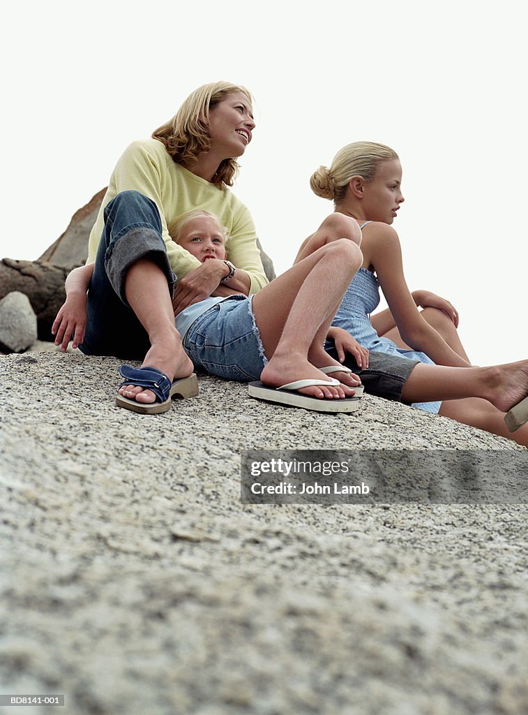 Woman and two girls (6-16) sitting on rocks