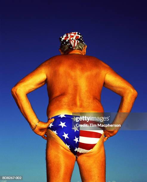 mature man wearing 'stars and stripes' swimming trunks, rear view - raya del bronceado fotografías e imágenes de stock