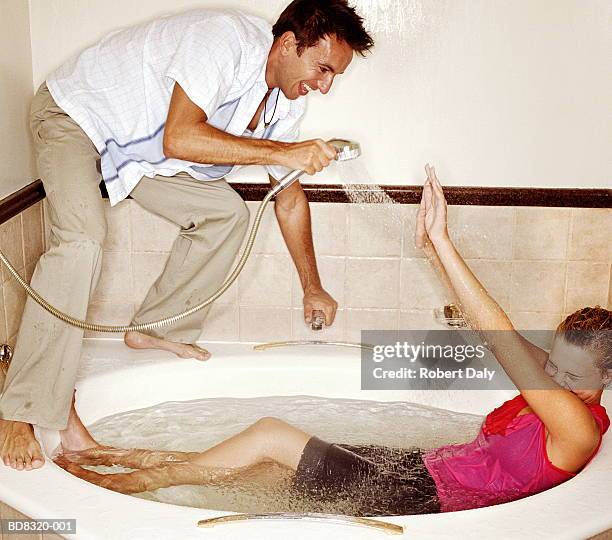 couple in bathroom fully clothed, man hosing woman with shower - shower man woman washing stock pictures, royalty-free photos & images