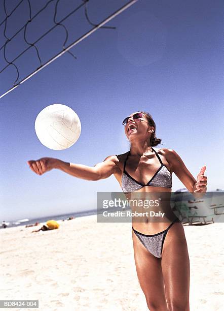 young woman wearing bikini striking volleyball on beach. - volleyball stock-fotos und bilder