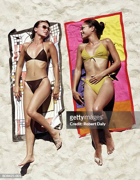 two young women chatting, sunbathing on beach, over head view - woman towel beach stock-fotos und bilder