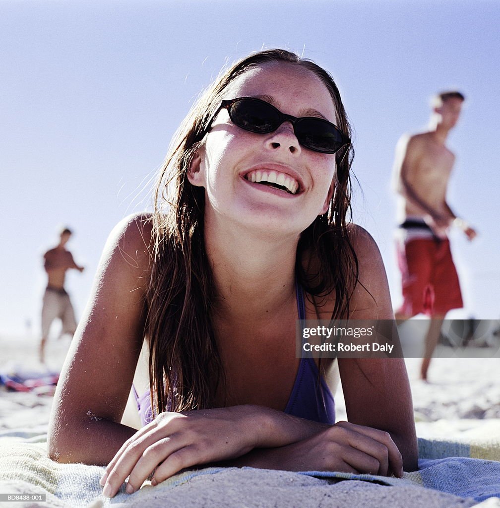 Young woman wearing sunglasses lying on beach, close-up