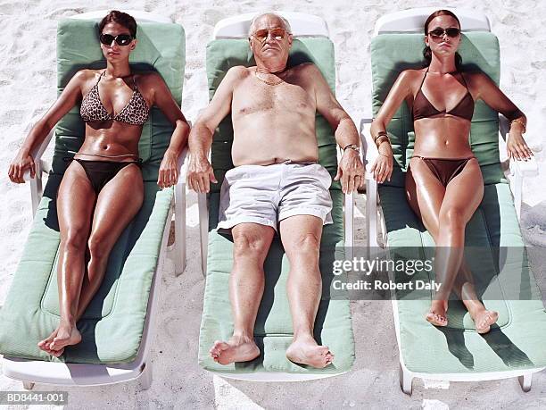 mature man and two young women on sun loungers on beach - apanhar sol imagens e fotografias de stock