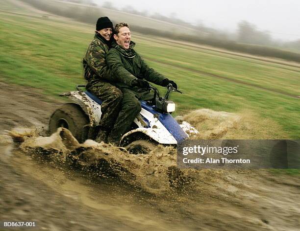 couple on quad bike driving through muddy puddle - quad foto e immagini stock