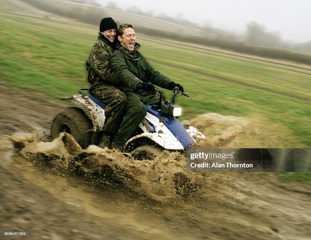 Couple on quad bike driving through muddy puddle