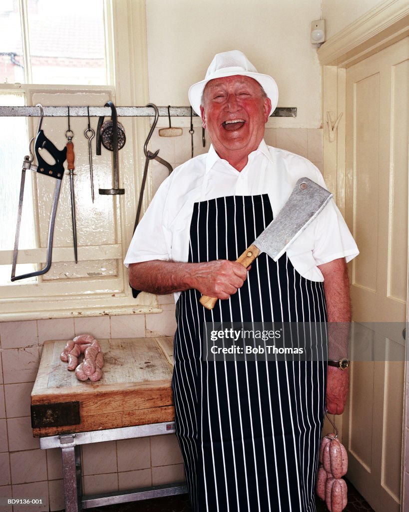 Mature male butcher holding sausages and meat cleaver, portrait