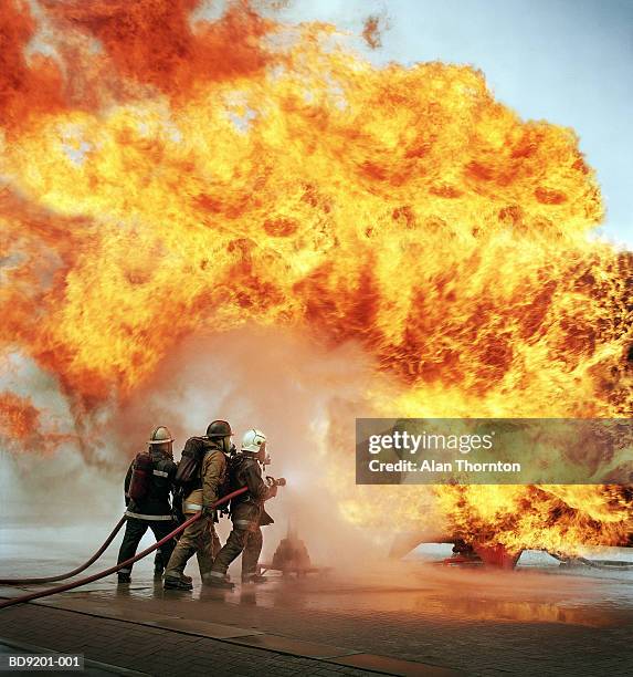 firemen with hose fighting firewall - flammenmeer stock-fotos und bilder
