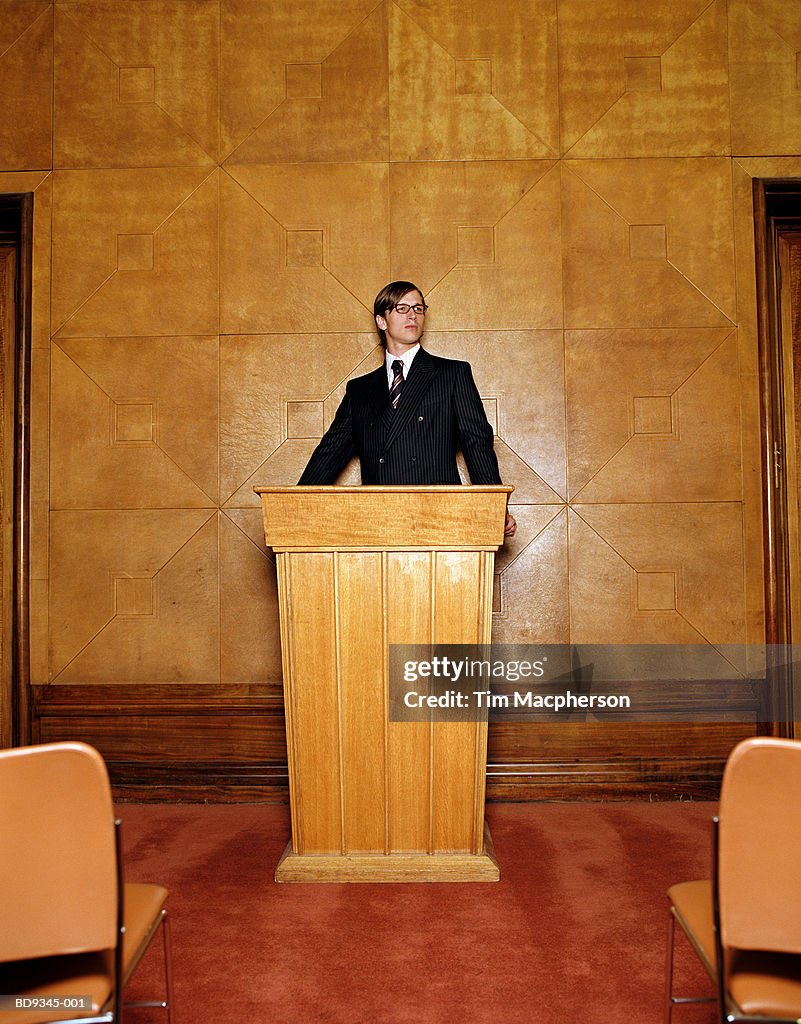 Young man wearing suit and glasses standing at lectern