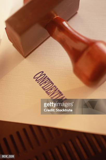 rubber stamp resting on paper with confidential stamped on it - stamp foto e immagini stock