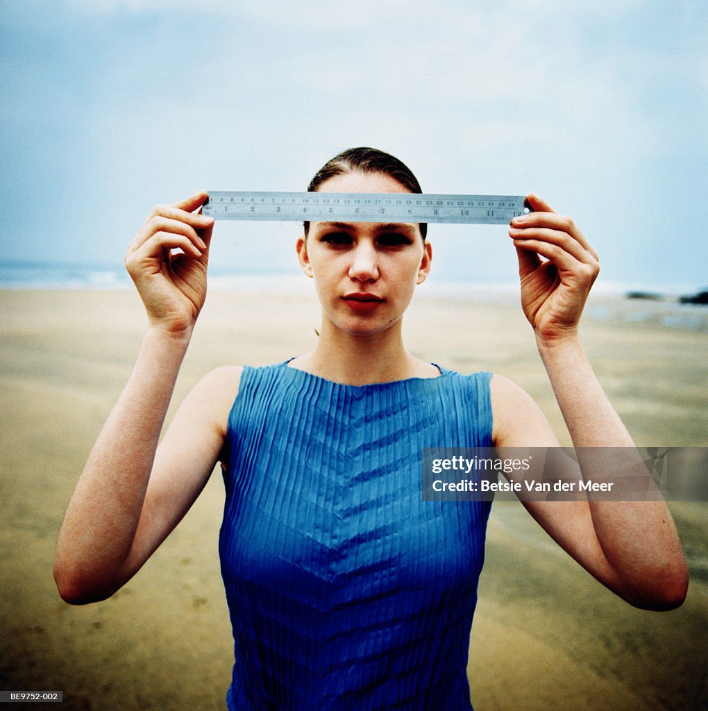 Young woman on beach holding ruler, portrait