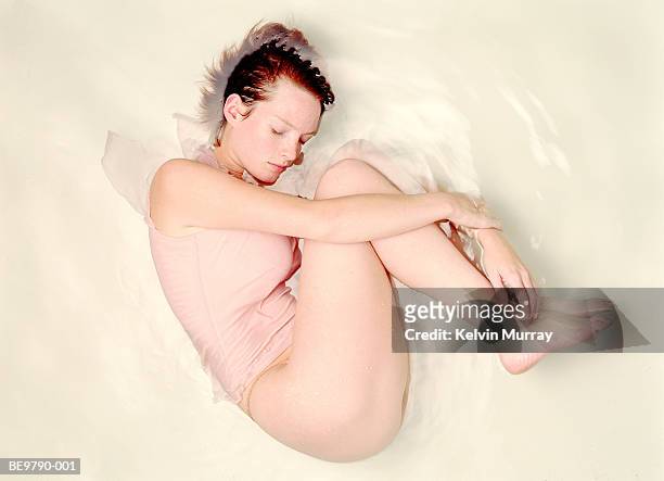semi-naked woman in foetal position, part submerged in water - halbbekleidet stock-fotos und bilder