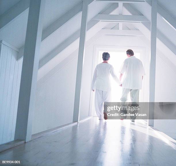 mature couple walking down corridor holding hands, rear view - nah stock-fotos und bilder