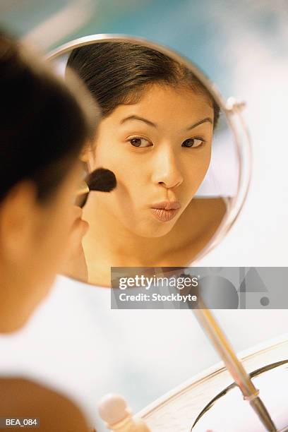 woman looking at reflection in mirror and applying blush - pincel de blush imagens e fotografias de stock