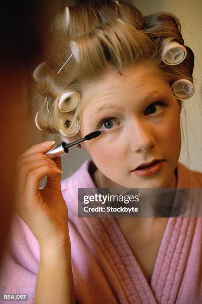 woman applying mascara, wearing bathrobe, curlers in hair - hair curlers stockfoto's en -beelden