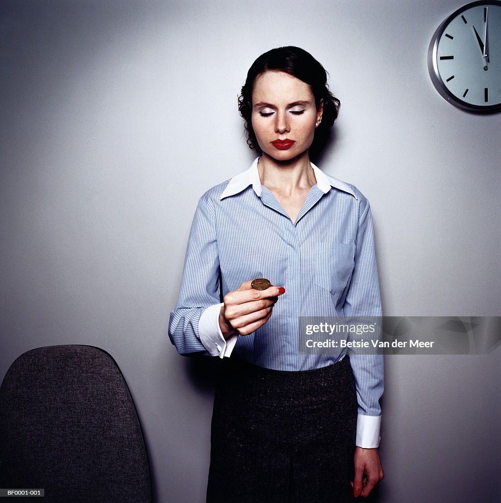 Businesswoman about to flip coin, eyes closed, portrait